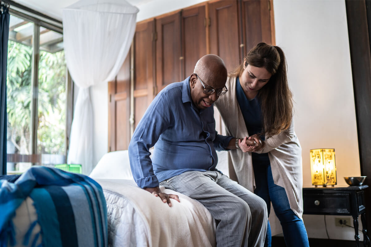 Home caregiver helping a senior man standing up at home